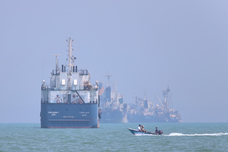 A small motorboat with a few people on it passes past four large ships on a body of water.