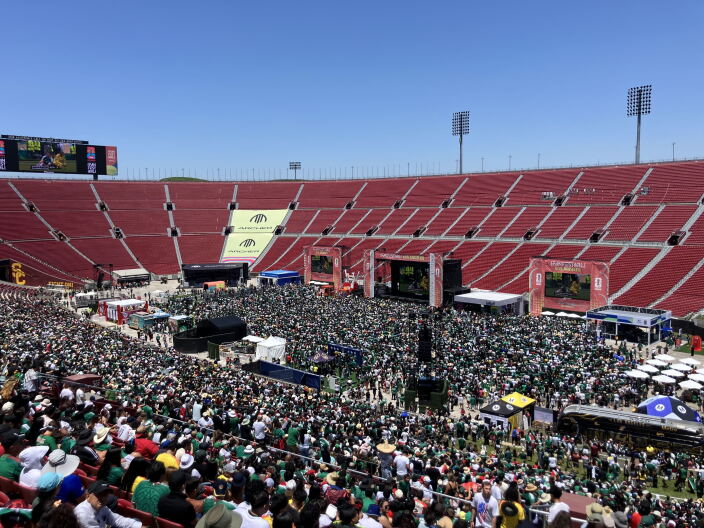 A large crowd of people inside a stadium with multiple large screens. 